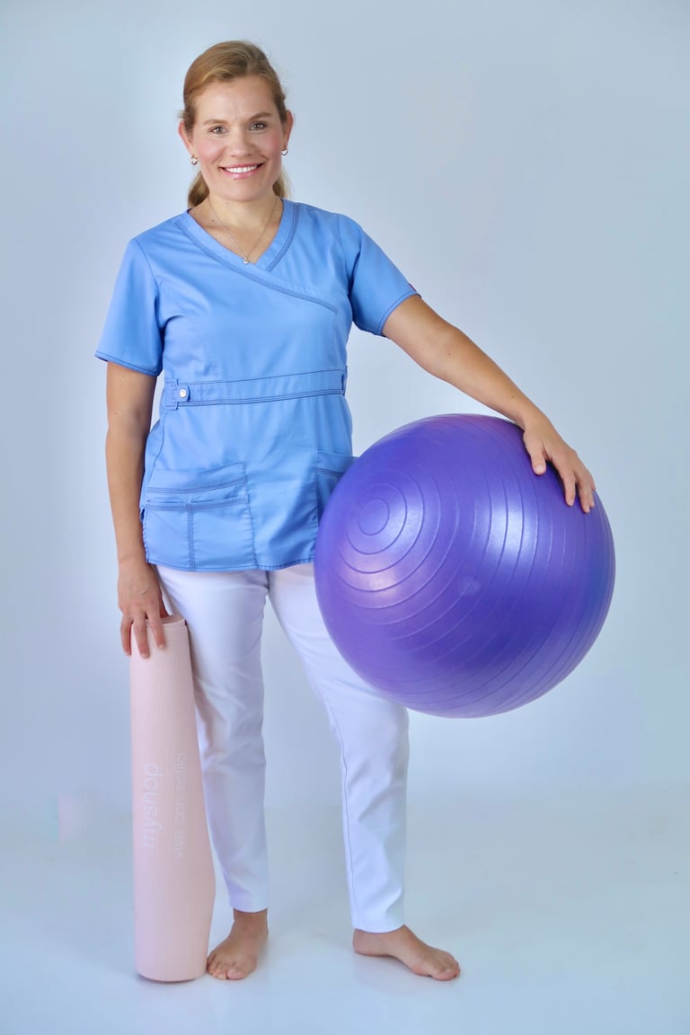 Female physical therapist in blue scrubs holding a purple exercise ball against a light background